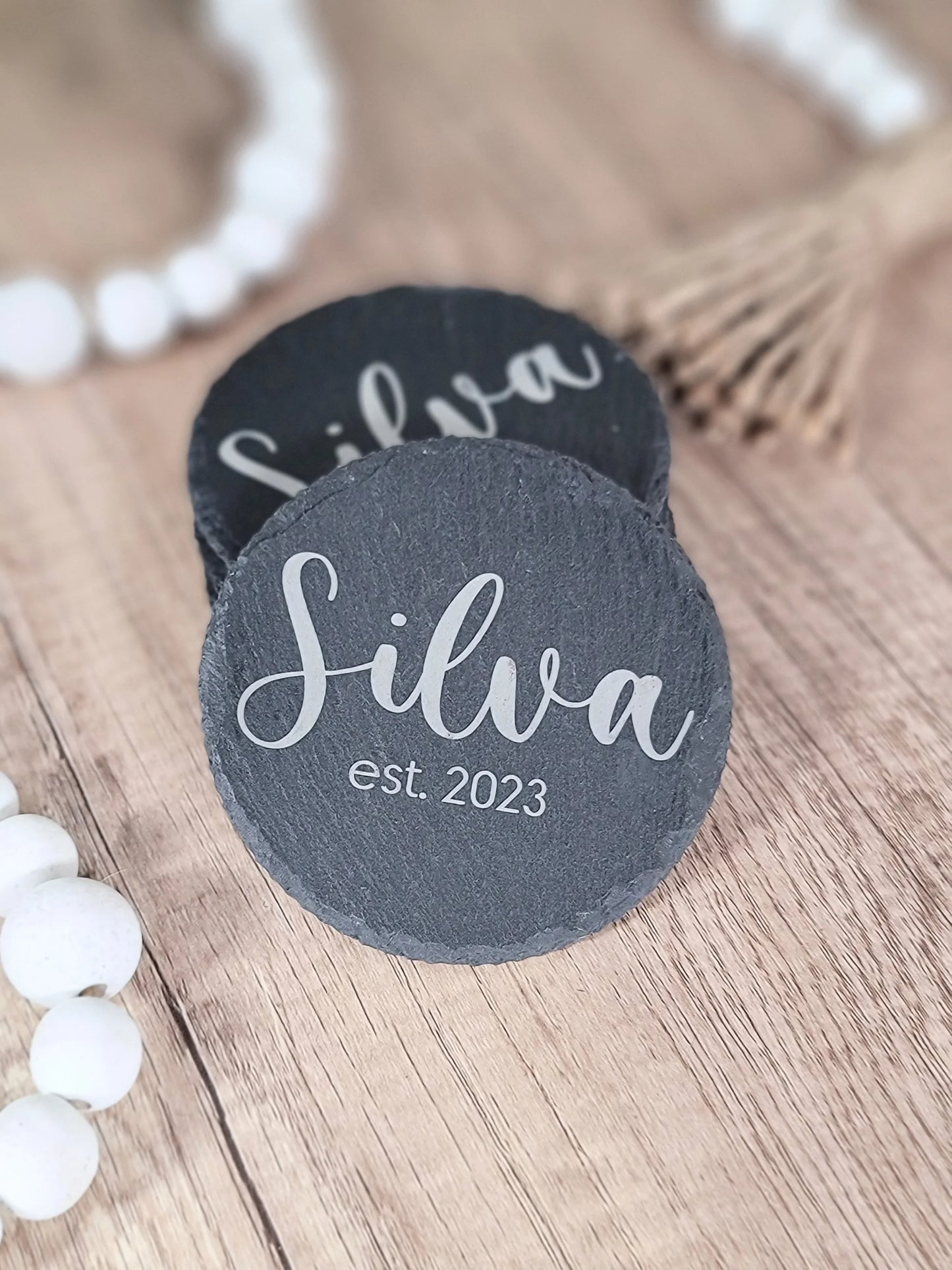 Personalized slate coaster engraved with 'Silva est. 2023' on wooden surface