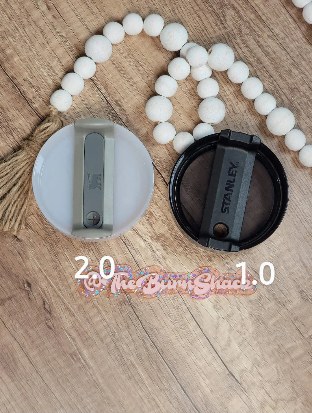 Comparison of two Stanley tumbler lids, 2.0 and 1.0 versions, on wood background.
