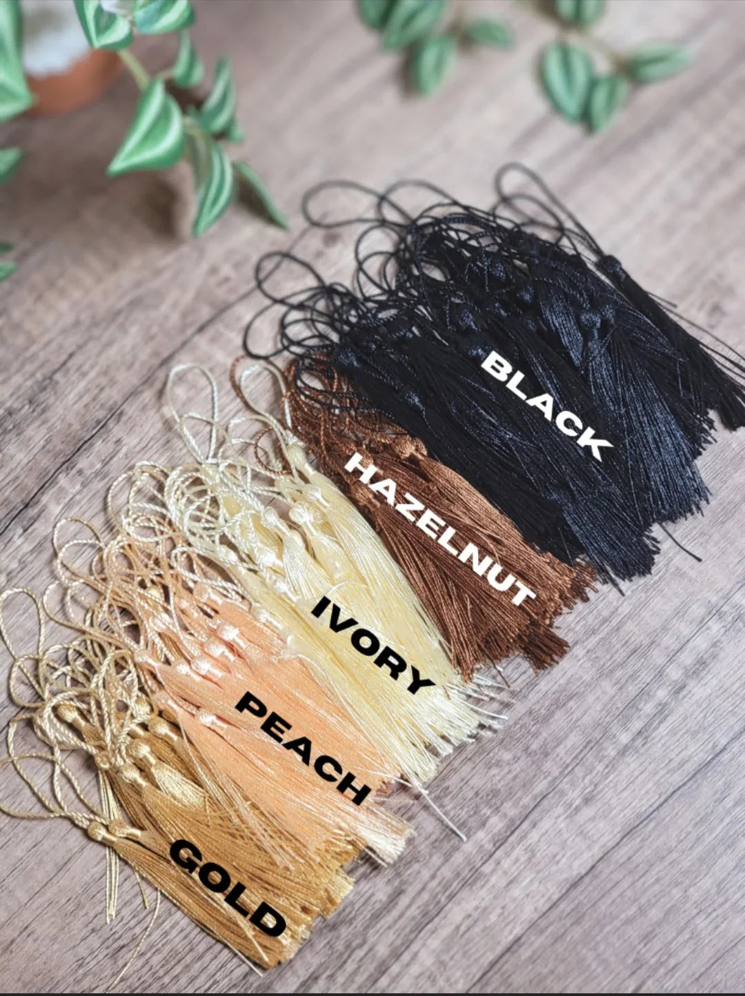 Assorted tassels in black, hazelnut, ivory, peach, and gold colors on wood surface