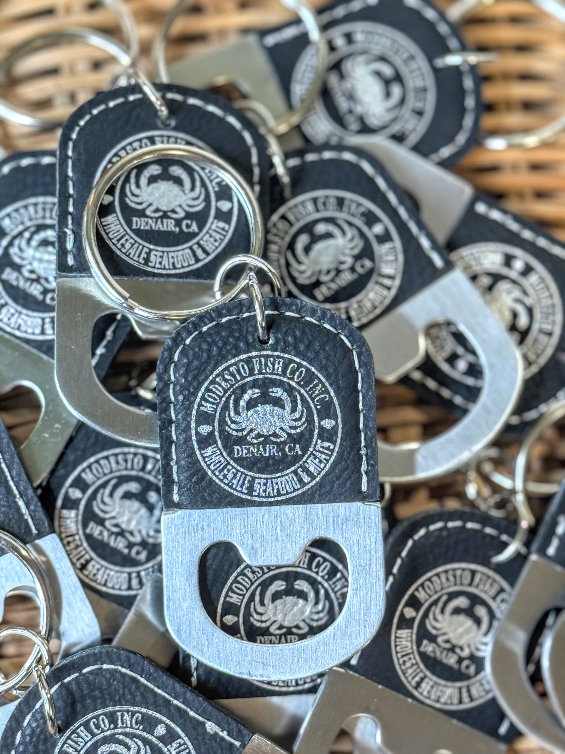 Custom laser engraved black vegan leatherette bottle opener keychain with silver engraved circular logo — personalized corporate gift by The Burn Shack, Denair CA